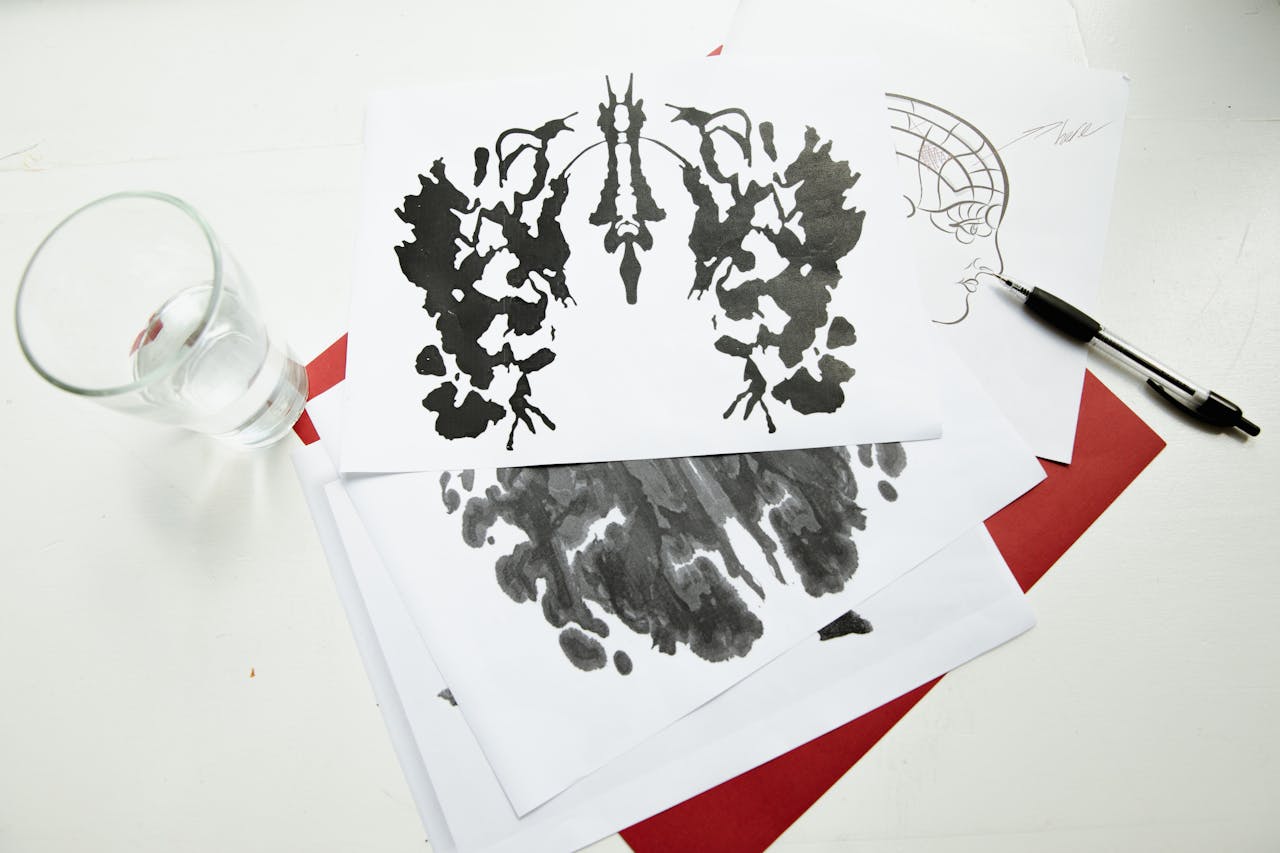 heros-img An artistic arrangement of inkblot test sheets with a pen and glass on a table.